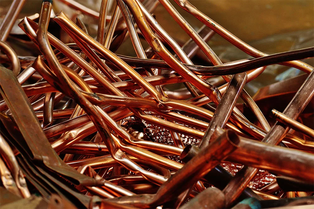 Cette image montre un amas de morceaux de cuivre brillants, probablement des chutes de matériau recyclable, entremêlés et réfléchissant la lumière, créant une texture riche en détails et en couleurs. | Achat de métaux- Recyclage LGI