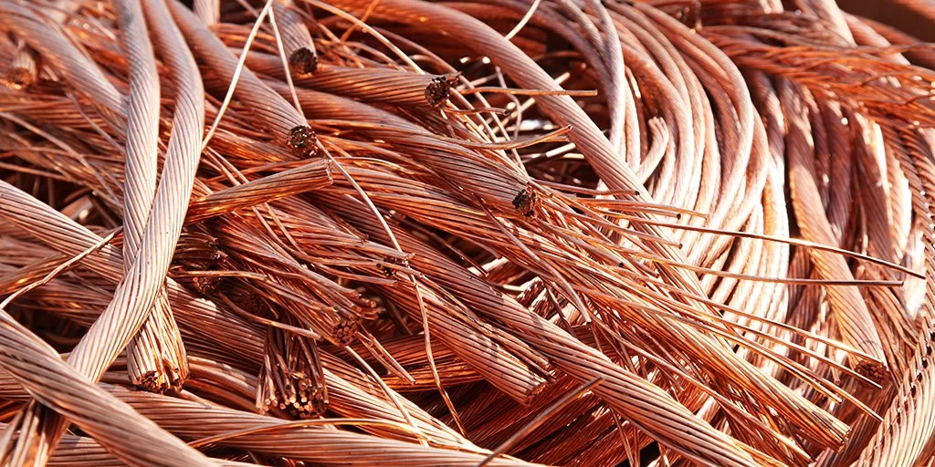 Cette image montre de près un enchevêtrement de fils de cuivre. Les fils, fins et torsadés, présentent une couleur cuivrée brillante et sont disposés en boucles et enroulements complexes qui captent la lumière, soulignant leur texture et leur éclat métallique. | Recyclage de métaux - Recyclage LGI
